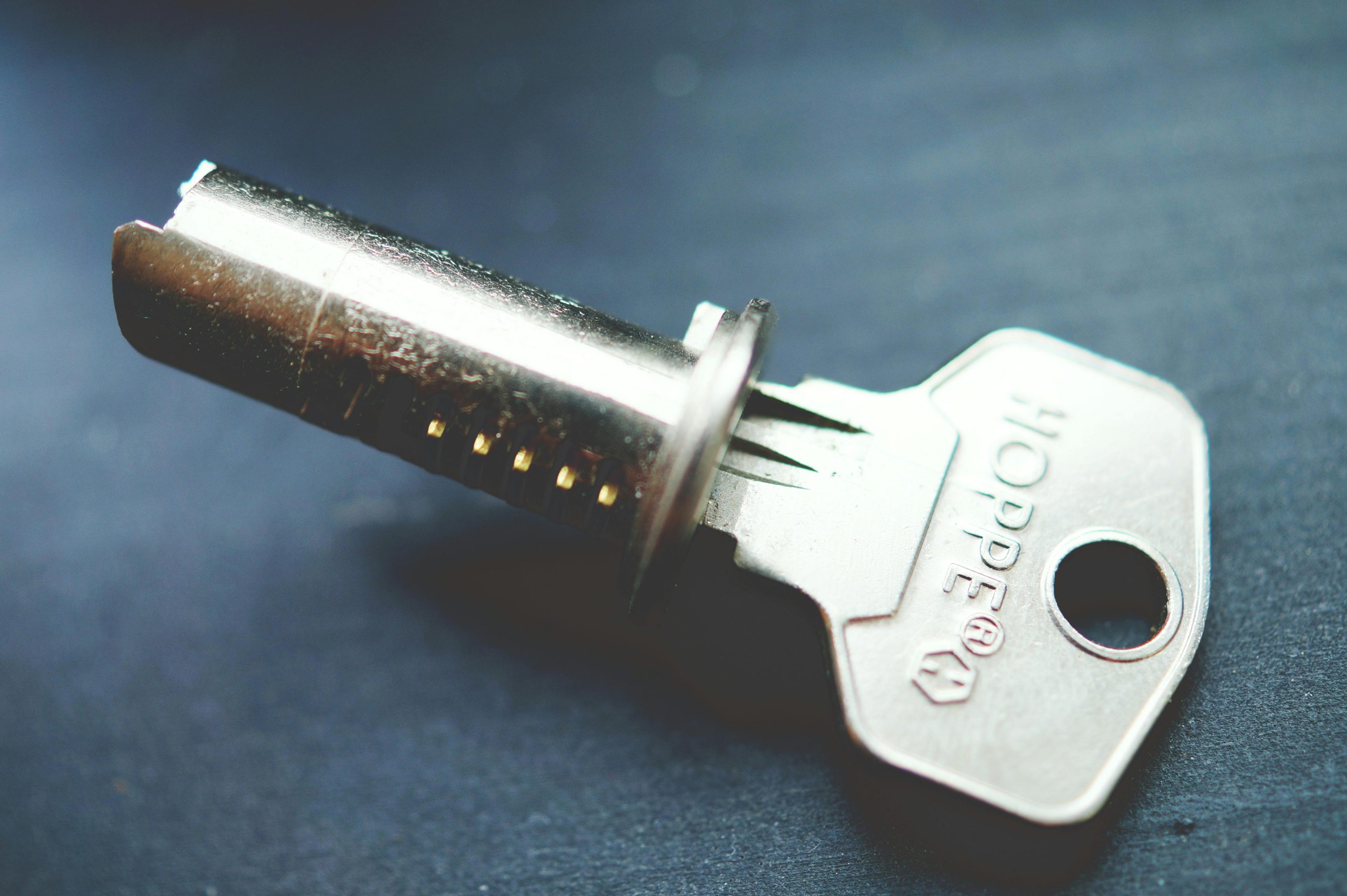 Home Detailed close-up image of a metallic key with lock cylinder on a dark surface, highlighting intricate details.