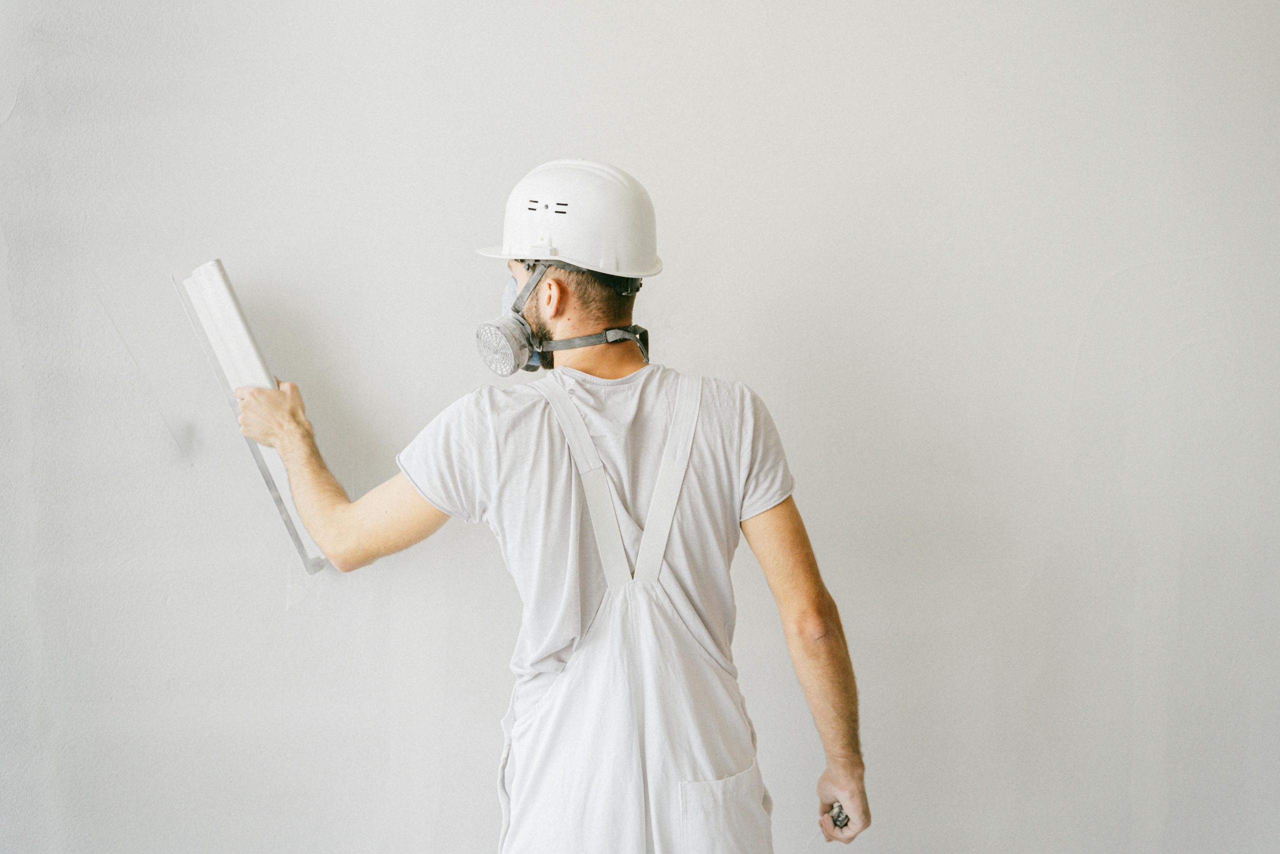Home Back view of a construction worker in safety gear plastering a white wall.