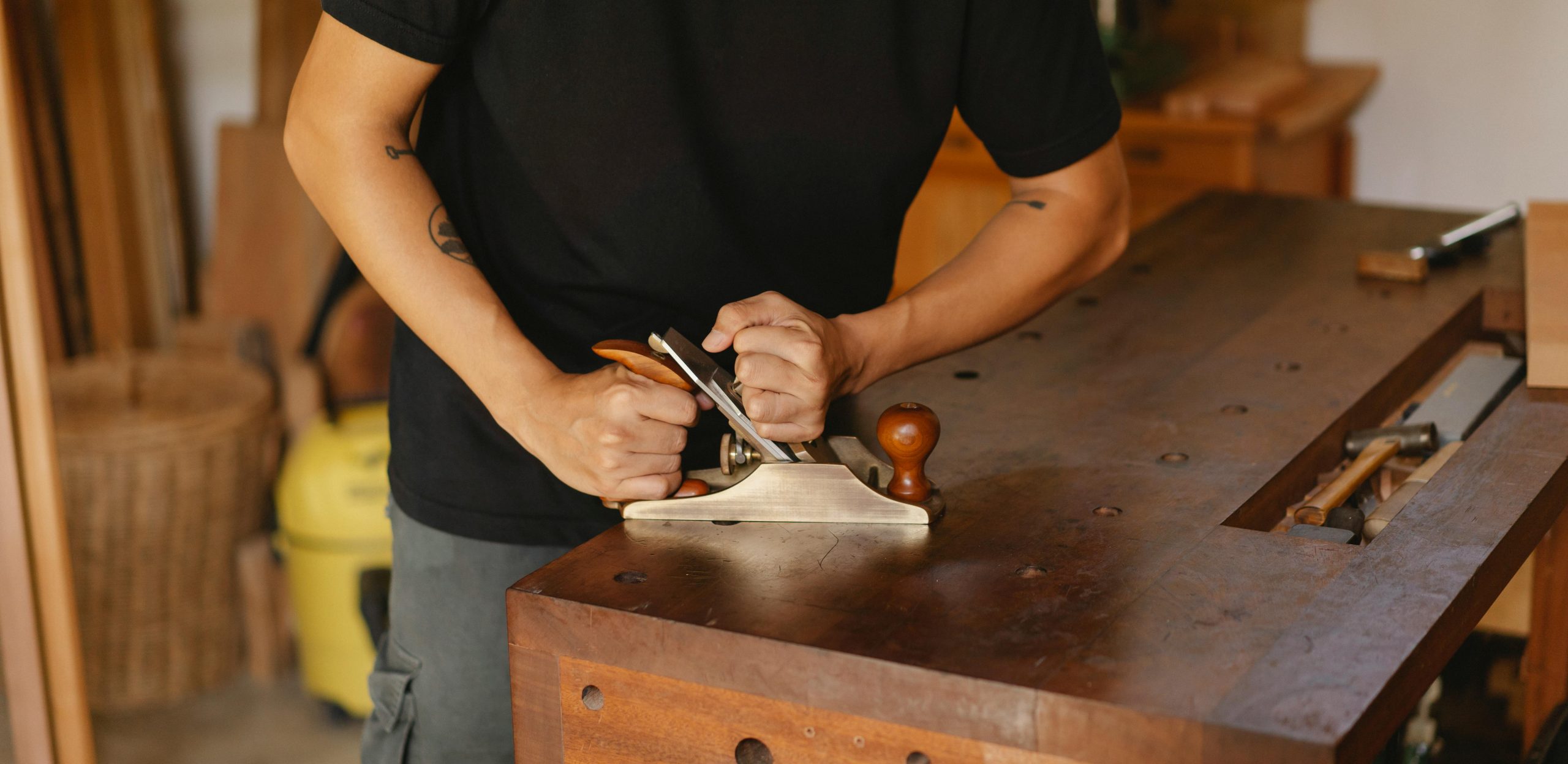 Home Woodworker focuses on smoothing wood with a planer in a cozy workshop setting.